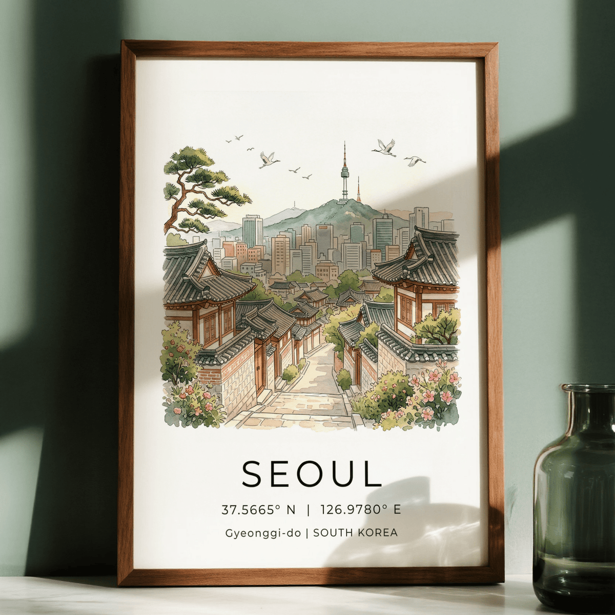 Framed Seoul Landscape Art Print showing traditional houses and skyline with birds against a green wall with a glass jar nearby