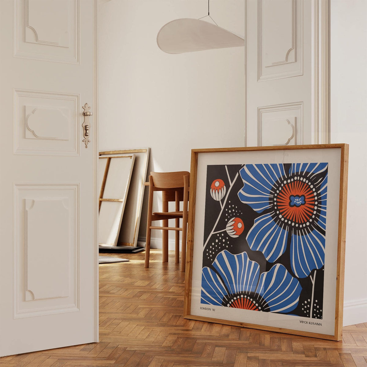 Flowers prints leaning on floor with blue poppy flowers in minimalist style and wooden chair in background