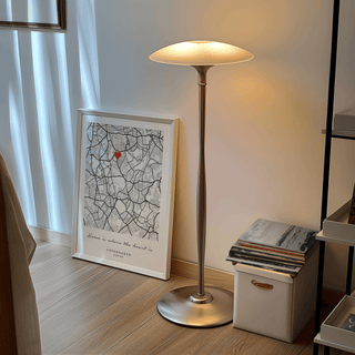 Print leaning on the floor with city map and red heart next to a lit floor lamp and stack of books