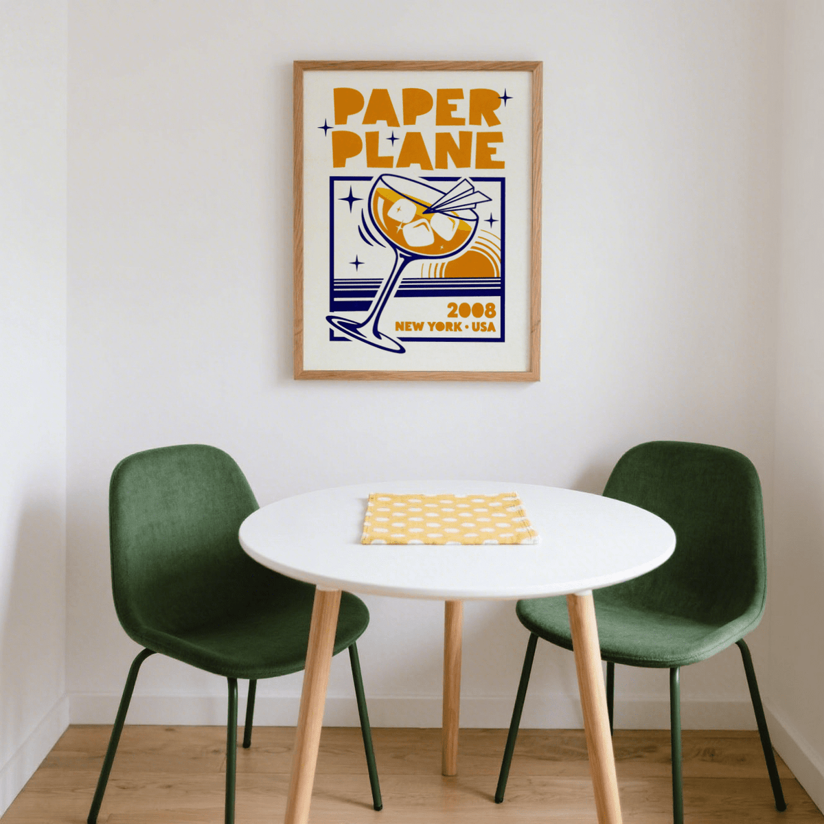 Paper Plane Cocktail Poster print on a wall above a white round table with green chairs and wooden floor