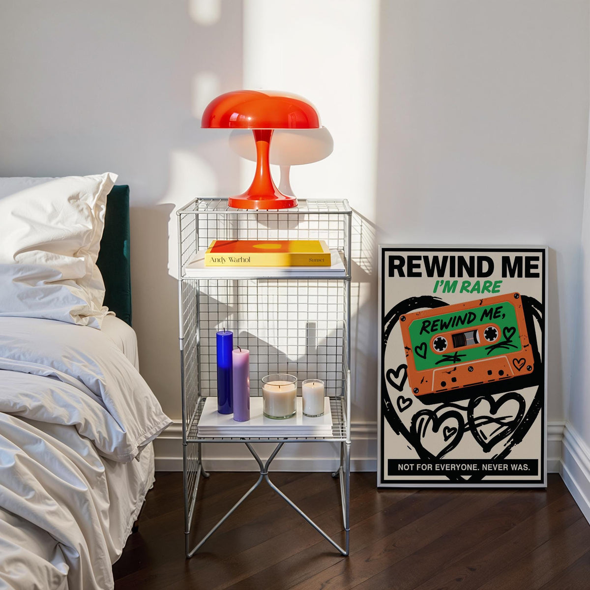 Retro cassette wall art with orange and green colours leaning against a wall beside a wire shelf and a red lamp