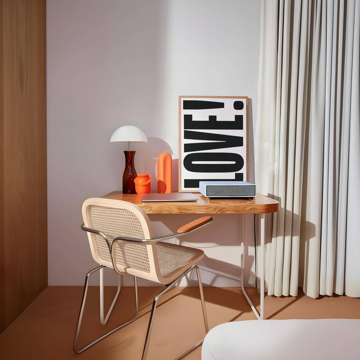 Print leaning on a desk of LOVE typography with a beige chair and white curtains