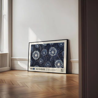 Landscape poster of dandelion seed heads in a black frame leaning on a parquet floor near a window