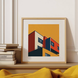 Framed Bauhaus Architecture print of an abstract building in orange and red tones on a shelf beside stacked books