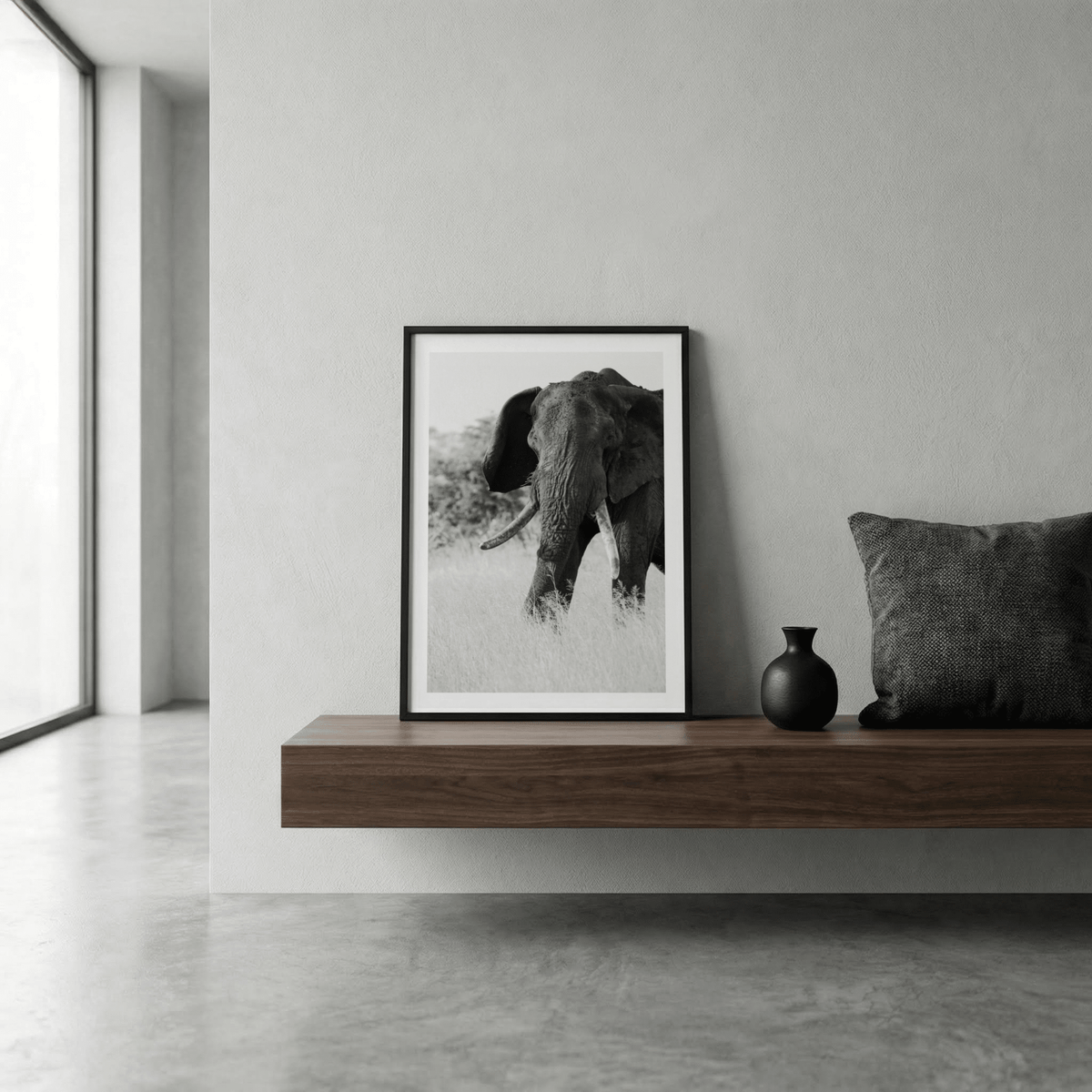 Elephant Black And White Art Print leaning on a wooden shelf with a black vase and dark grey cushion
