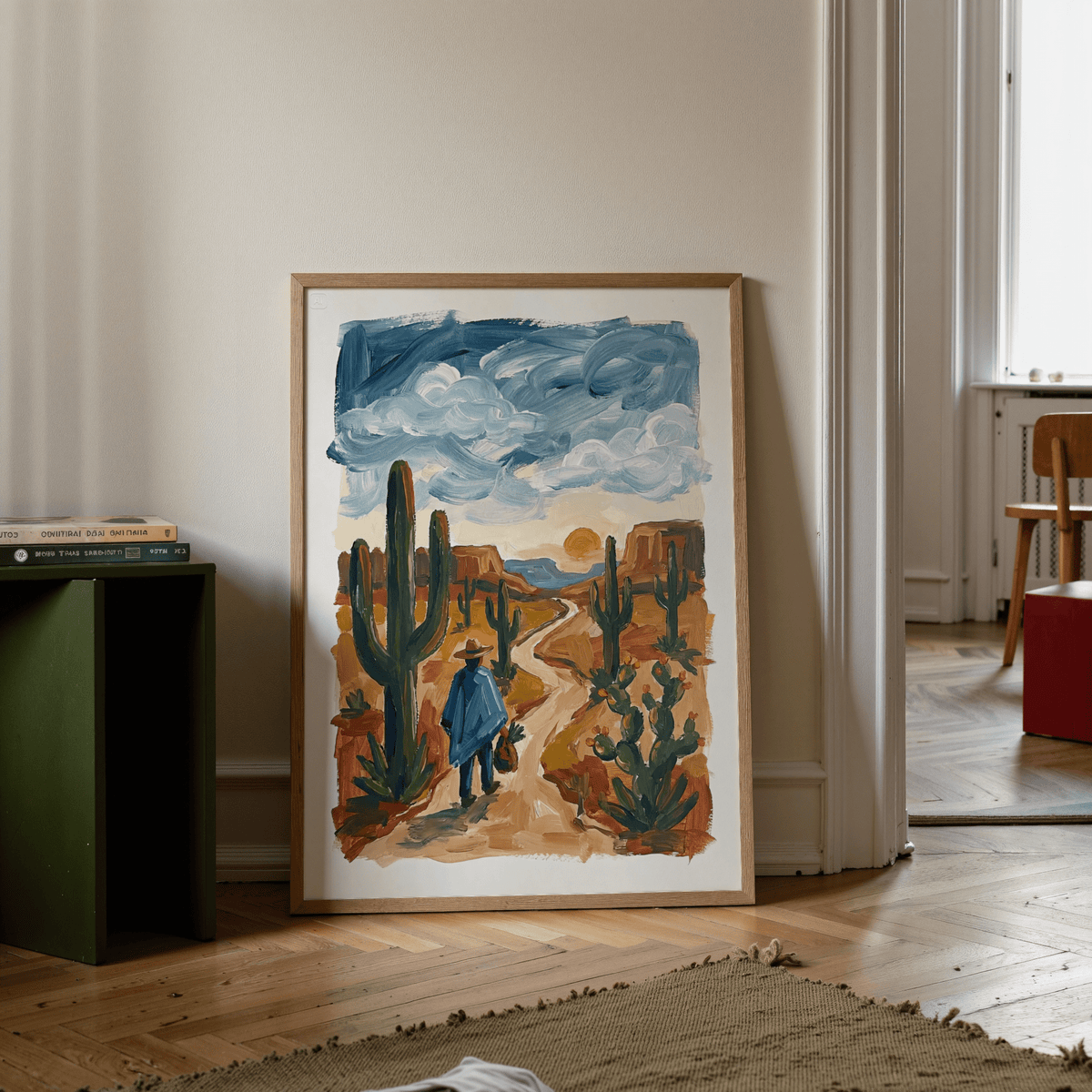 Print leaning on a floor of a figure walking in a desert with blue sky and orange earth next to green cabinet