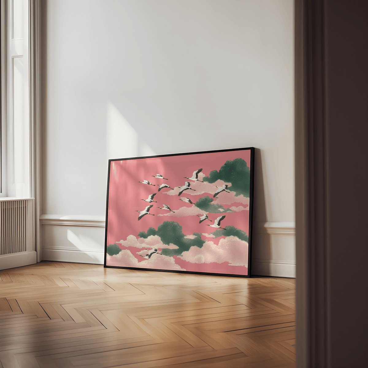Pink crane wall art leaning on a wooden floor with natural light and white walls