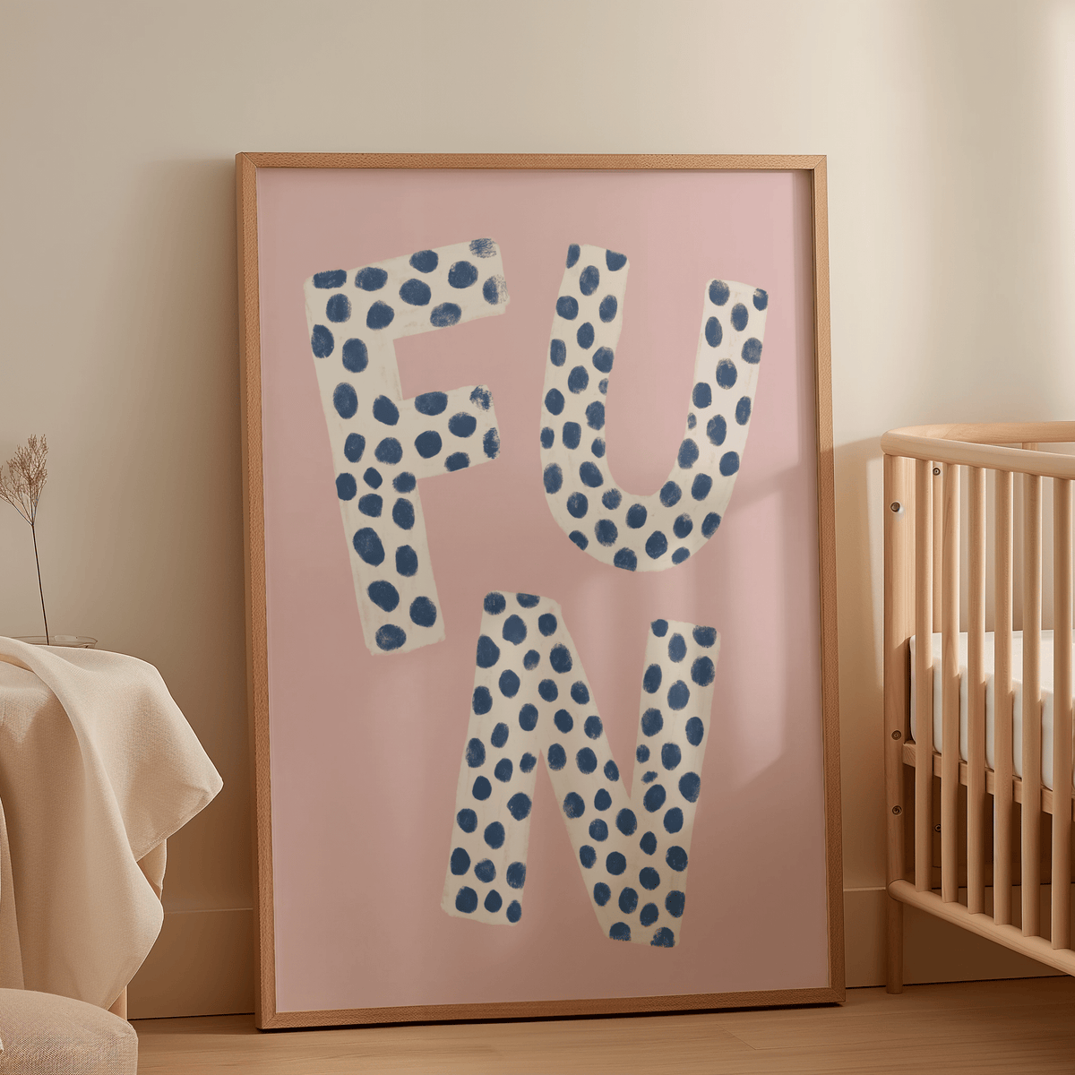 Fun typography wall art with white letters and blue dots on a pink background leaning in a nursery by a wooden crib