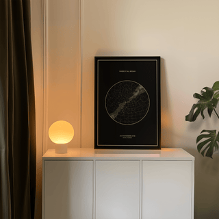 Custom Star Map print leaning on a white cabinet with a glowing lamp and plant nearby