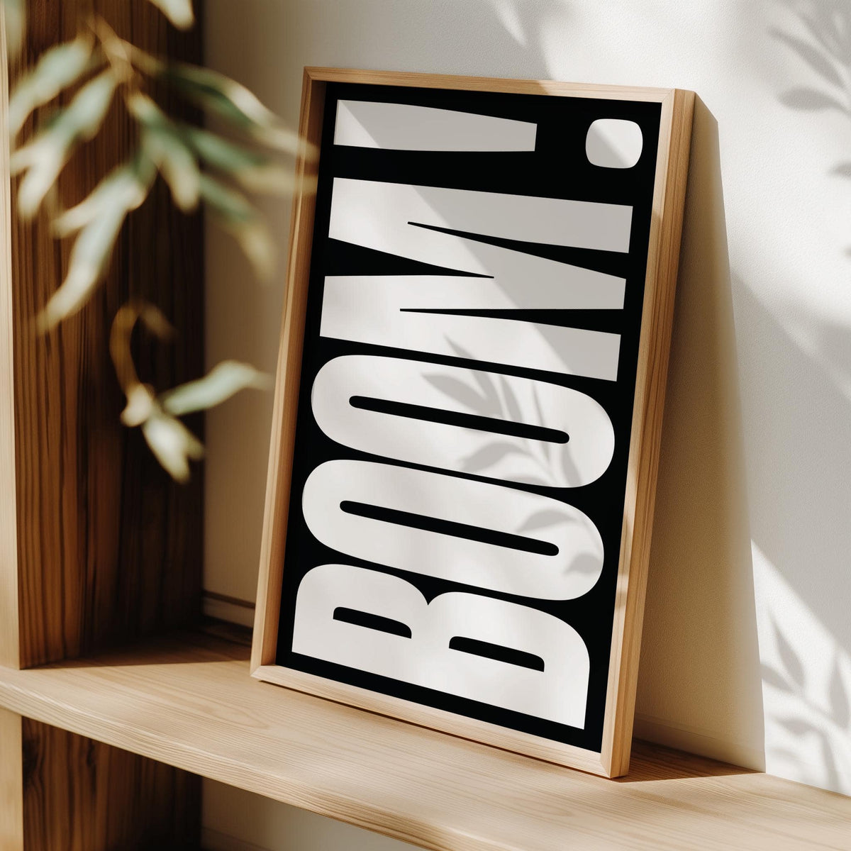 Framed print close-up of modern typography wall art with white BOOM text on black leaning on wooden shelf