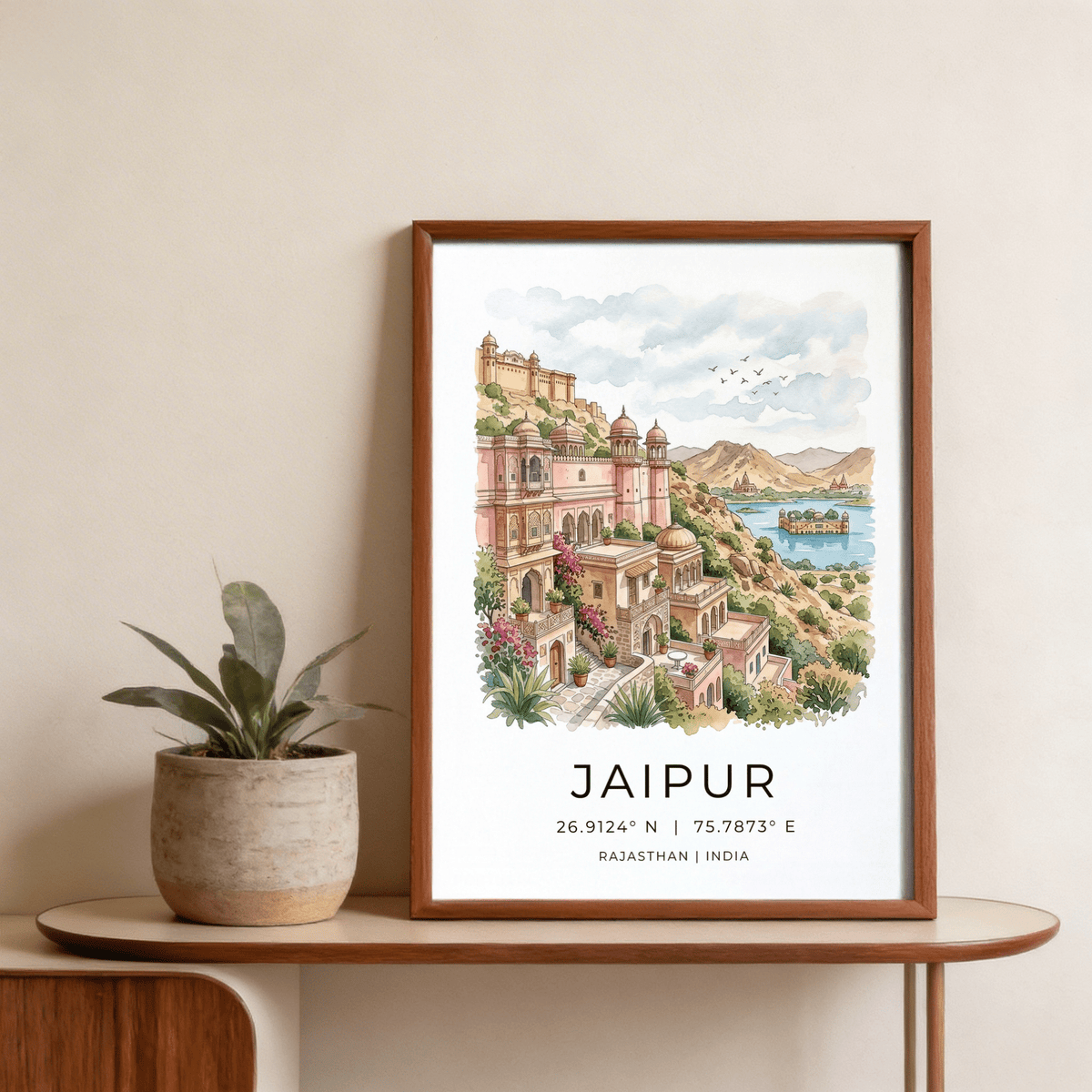 Framed Jaipur art print of a watercolour Jaipur cityscape with pink and green hues next to a potted plant