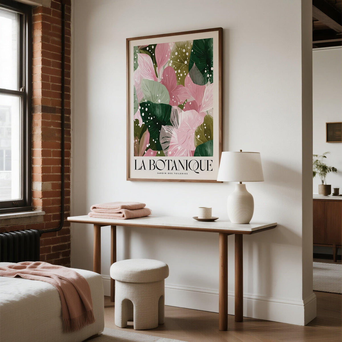 Print on a wall of decorative botanical leaves in pink and green above a table with a lamp