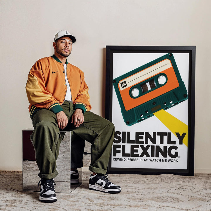 Cassette Poster leaning on the floor next to a man wearing a brown jacket and trousers