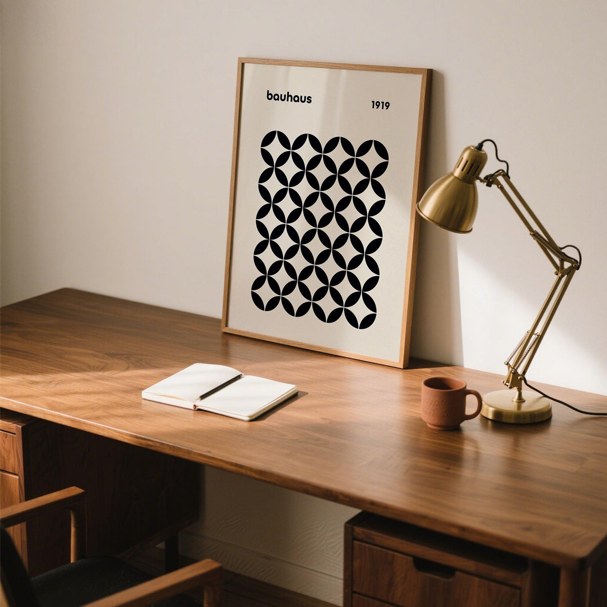Mid Century Wall Print leaning on a wooden desk with a brass lamp and open notebook in soft light