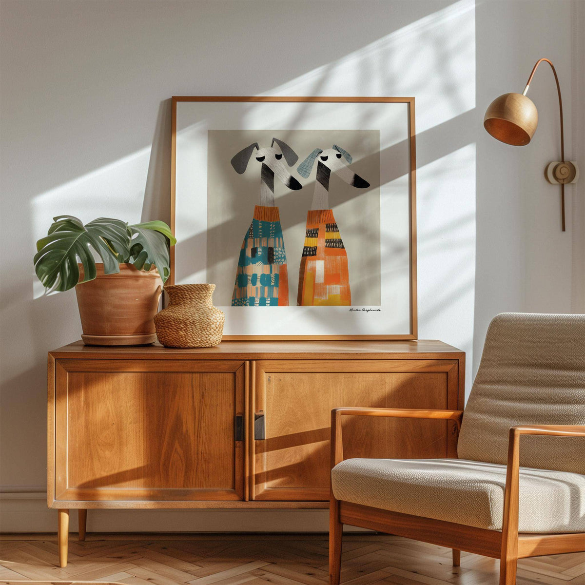 Wall art dog print of two greyhounds in colourful sweaters on a wooden sideboard with potted plants and lamp