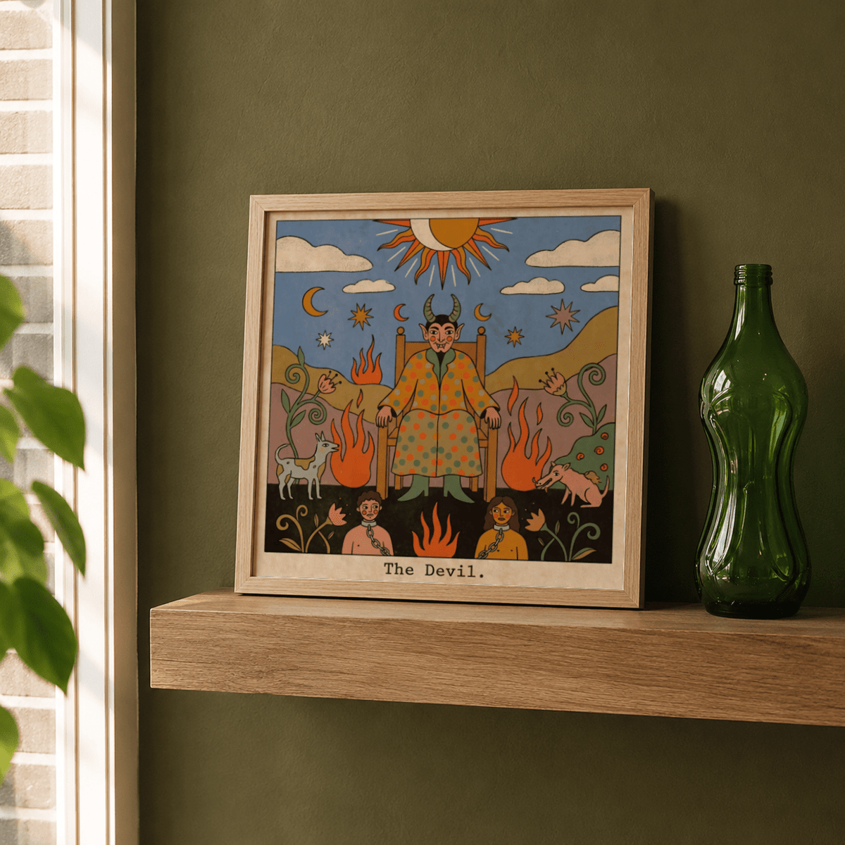 Print leaning on a shelf of Tarot Card Devil Art with folk-art illustration and muted colours beside a green glass bottle