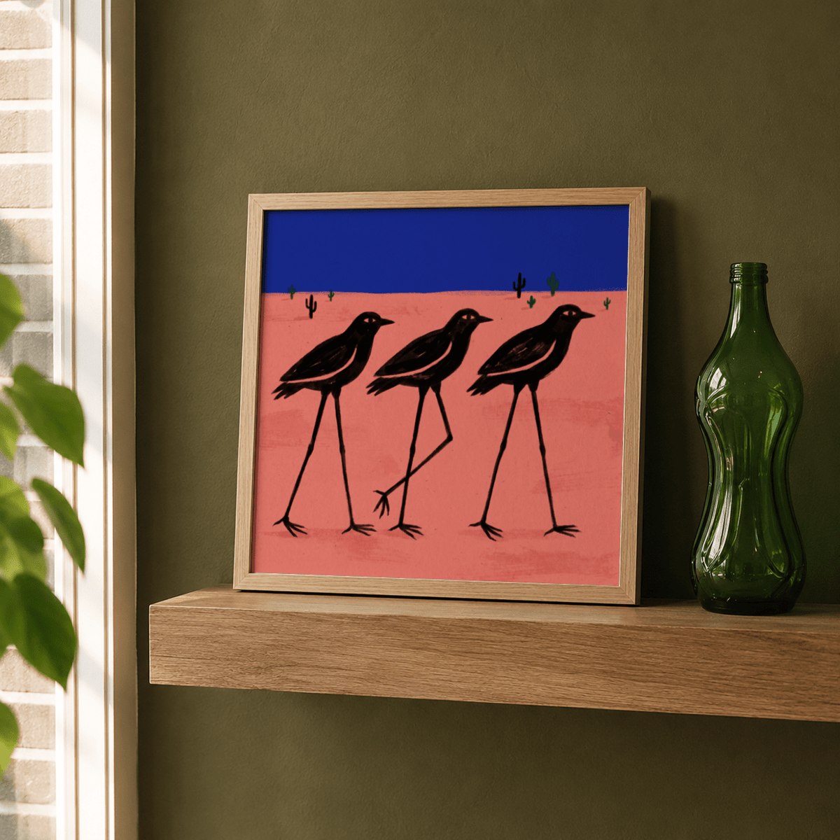 Desert Bird wall art with black stylised birds on pink and blue hues leaning on a wooden shelf next to a green bottle