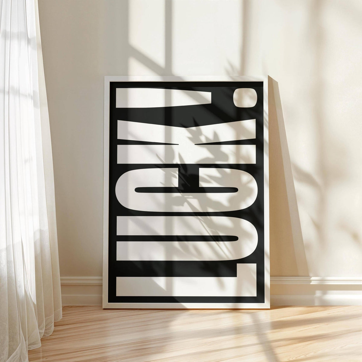 Print leaning on floor of minimalist black and white typographic word luck with window light and curtain