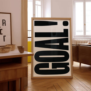 Print leaning on floor showing GOAL! typography in black on white with wooden furniture nearby