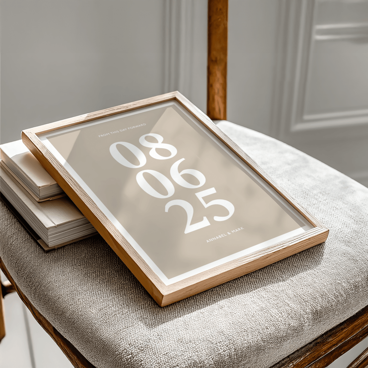 Framed Anniversary Date Print with beige background and white typography on a chair with books