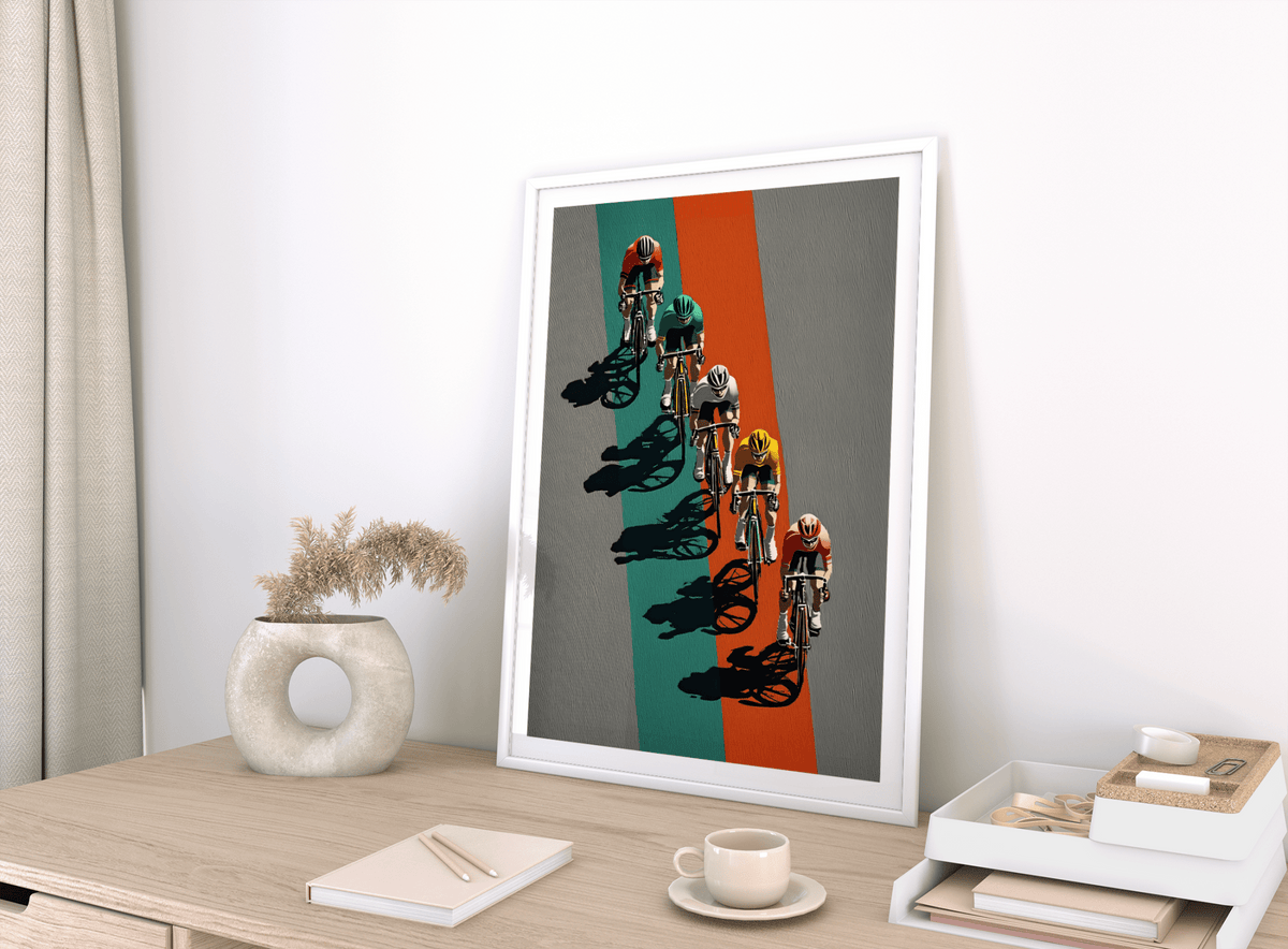Framed biking wall art of cyclists racing with green and orange lines leaning on a wooden desk next to a vase
