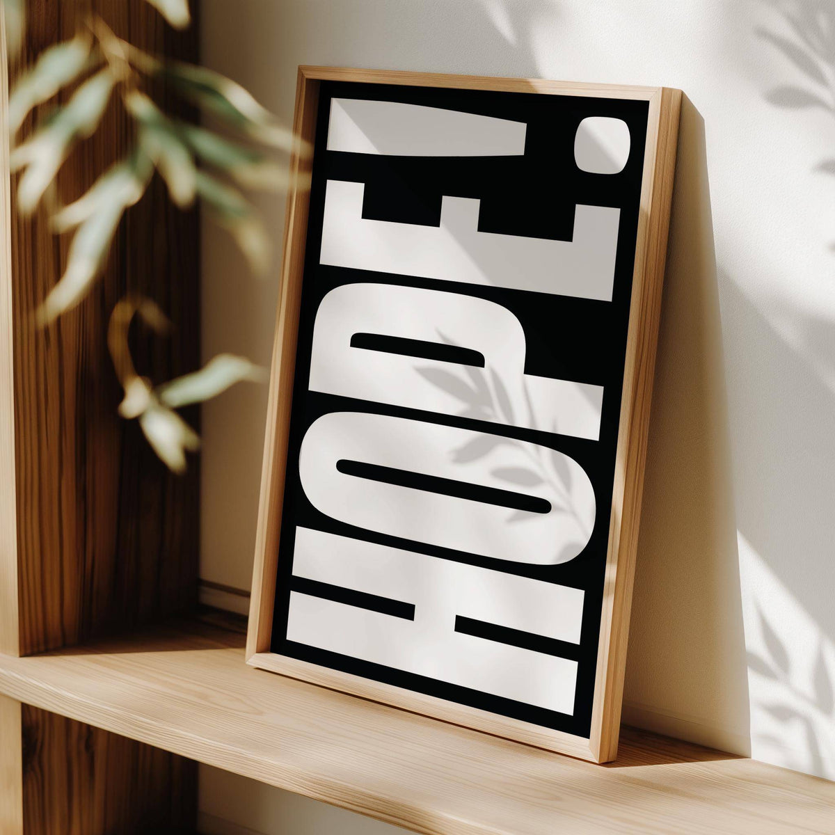 Framed print of Inspirational Artwork with bold white typography on black leaning on a wooden shelf
