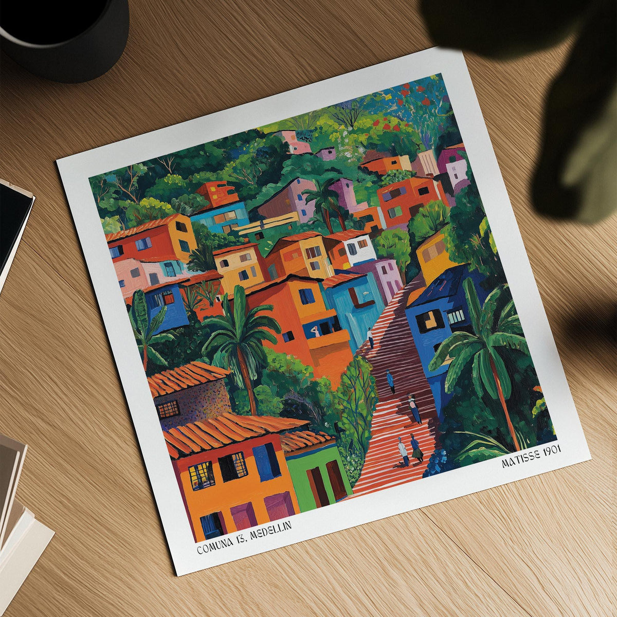 Comuna 13 Art print showing colourful hillside houses with lush green trees on a wooden surface next to a cup