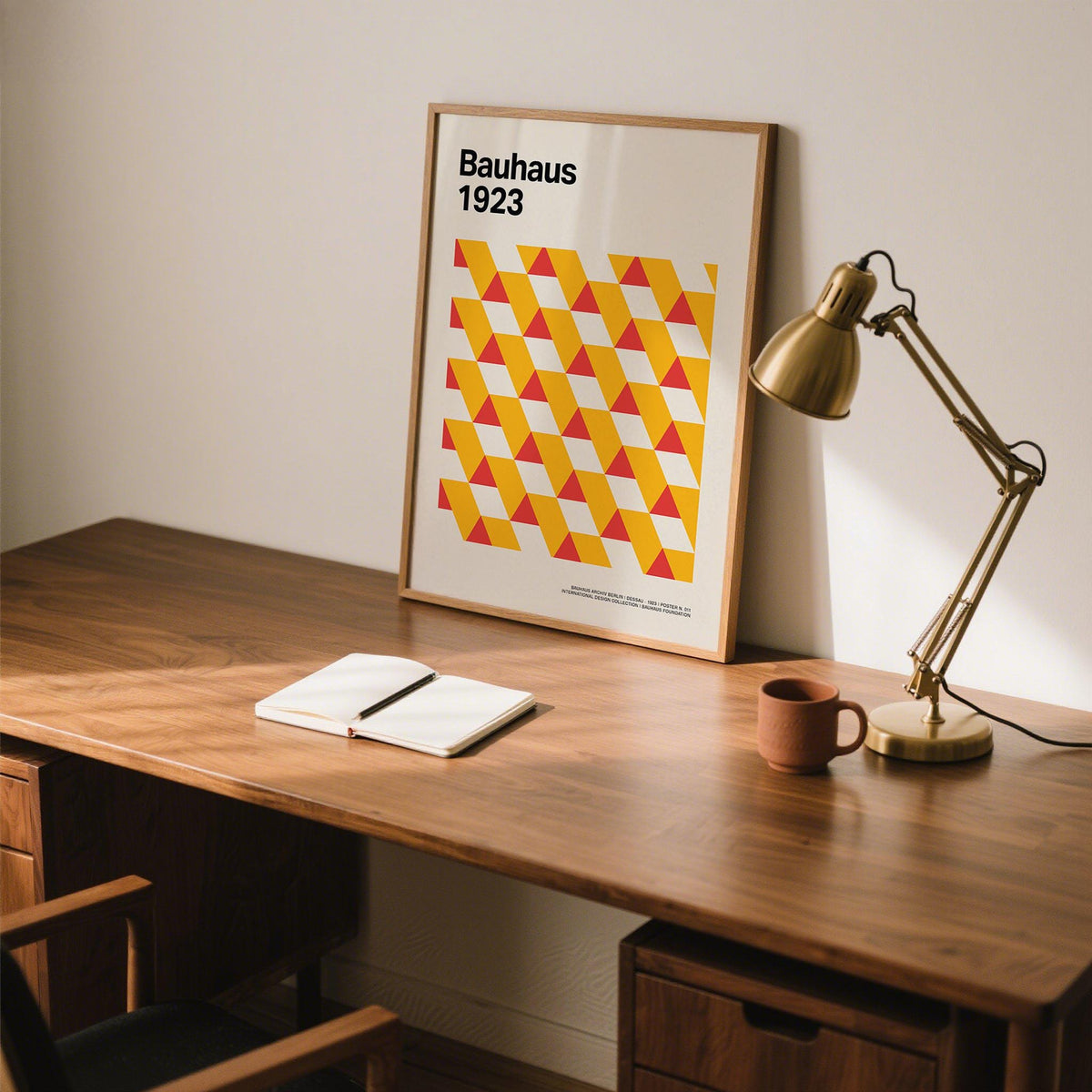 Art Posters Gallery print with minimalist yellow and red triangles leaning on a desk beside a brass lamp