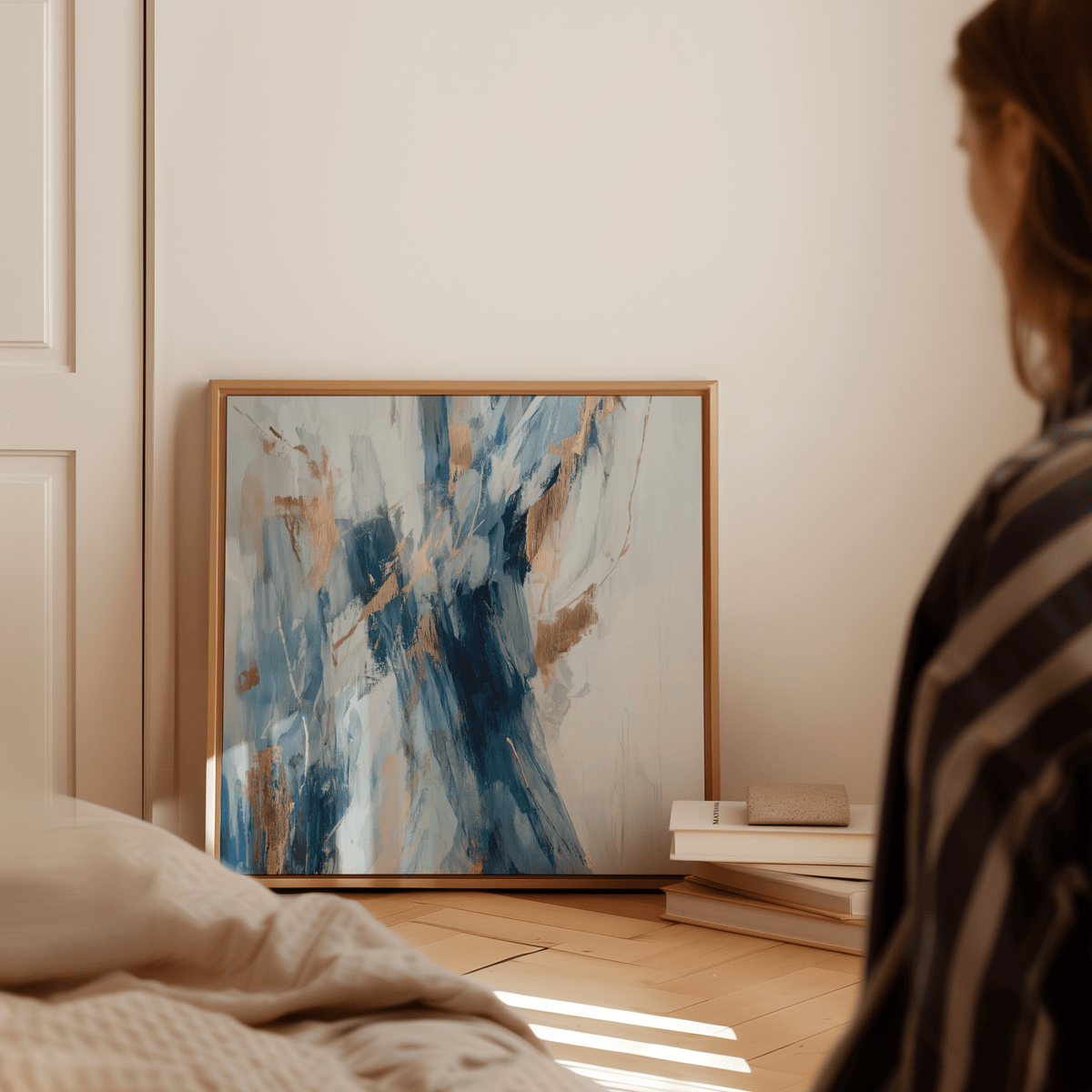 Abstract Blue Wall Art leaning on floor with blue and gold brushstrokes beside a book stack