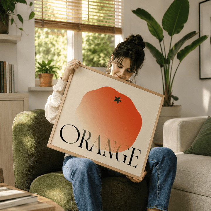 Framed close-up of minimalist fruit wall art with orange gradient and typographic text held by a woman
