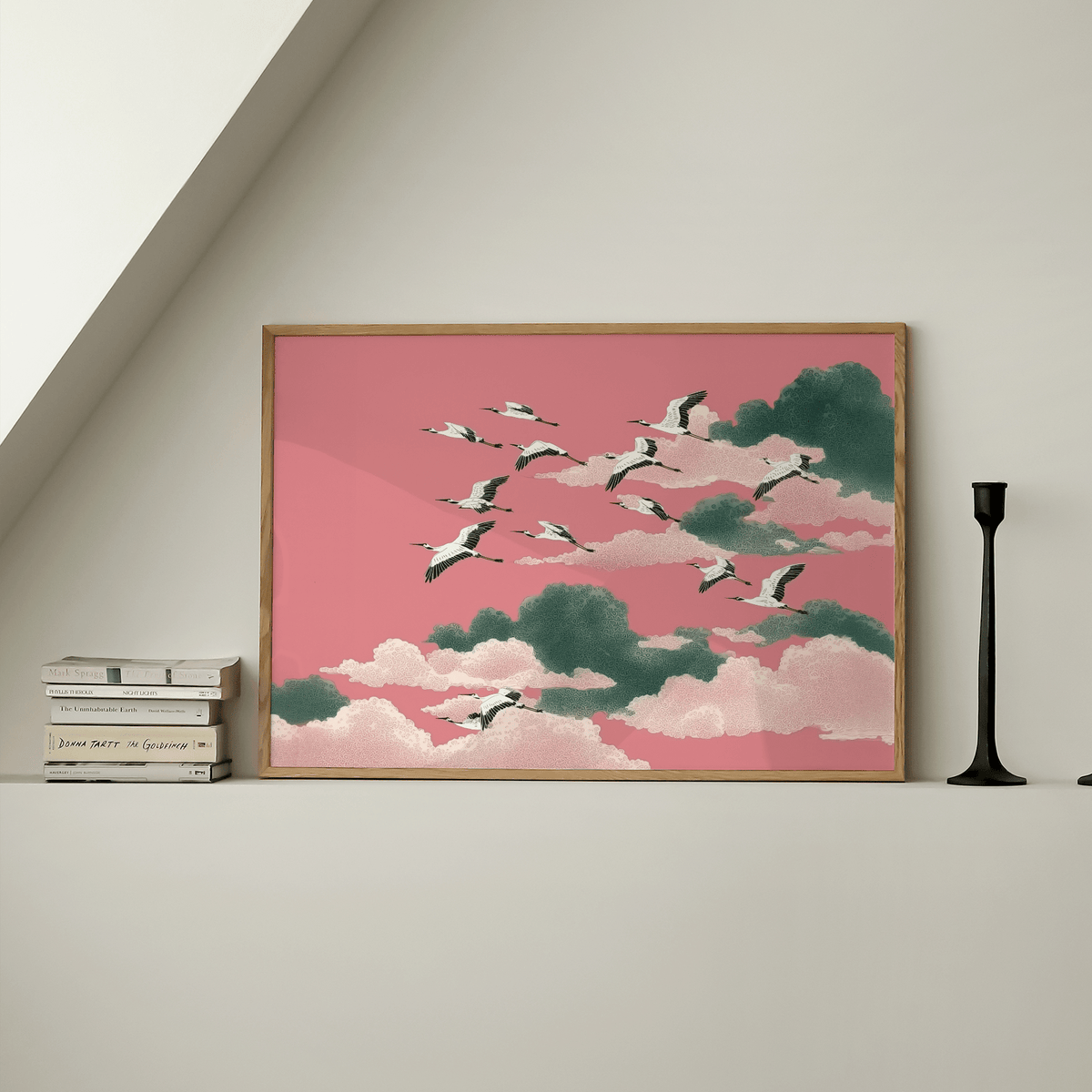 Framed Pink Crane Wall Art of flying cranes against pink and green clouds on a shelf with books