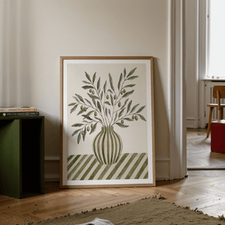Print leaning on the floor of olive branch art in green and beige tones near a dark green side table