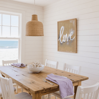 Love wall art with white calligraphy on beige background in a dining room with wooden table and purple napkins