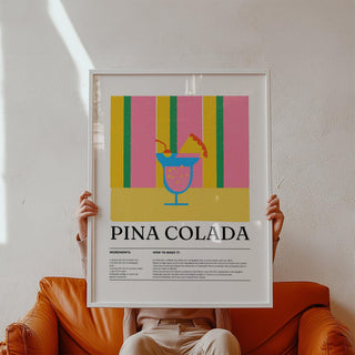 Framed print of piña colada cocktail illustration with colorful stripes held above a brown leather sofa