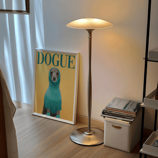 Print leaning on floor of dog in blue sweater with yellow background near lamp and books