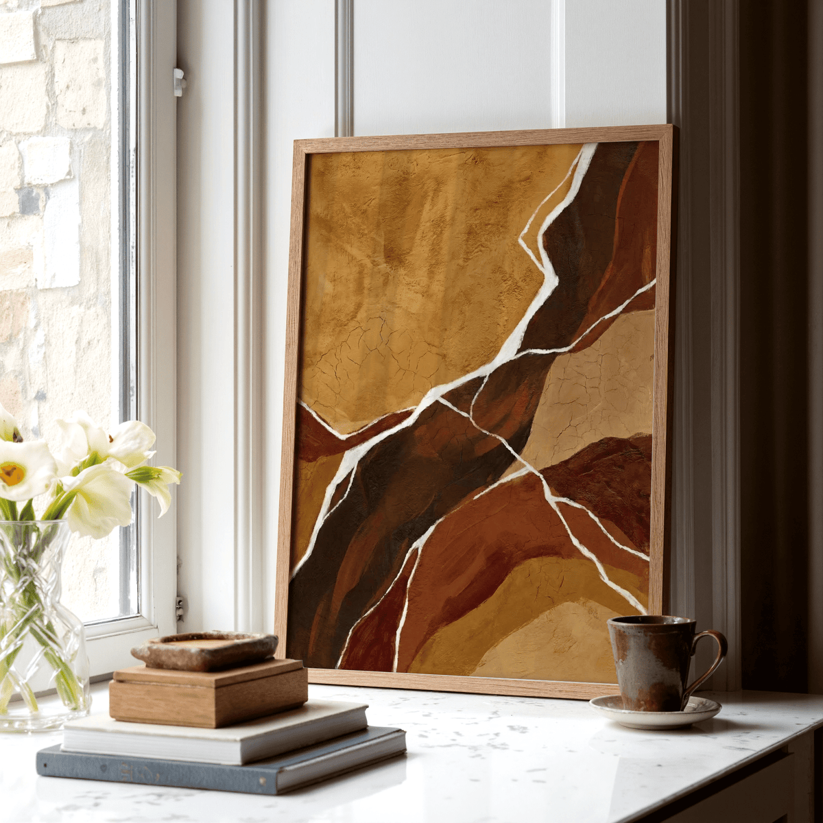 Print leaning on a shelf with abstract earth tones in brown and beige next to books and a cup