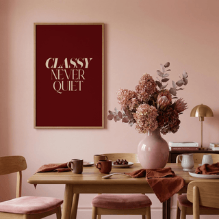 Classy wall art with beige text on burgundy above a dining table with pink chairs and a blush flower vase
