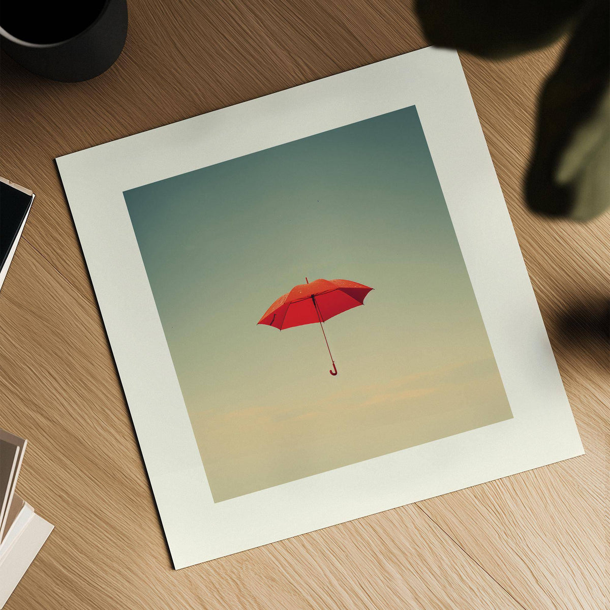 Close-up of surreal wall art showing a red umbrella floating against a muted sky on a wooden surface