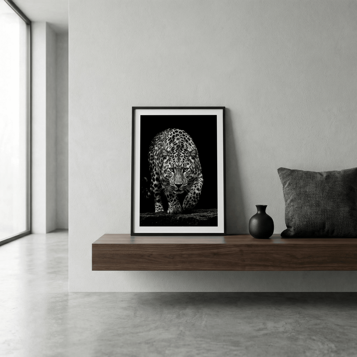 Print leaning on a shelf of a leopard in black and white with a black vase beside it