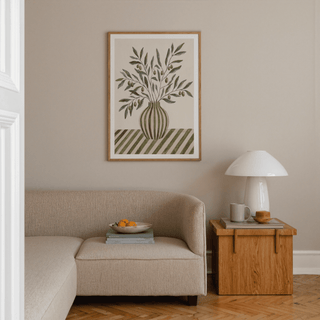 Olive Branch Art framed print on a beige wall above a corner sofa and wooden side table with lamp