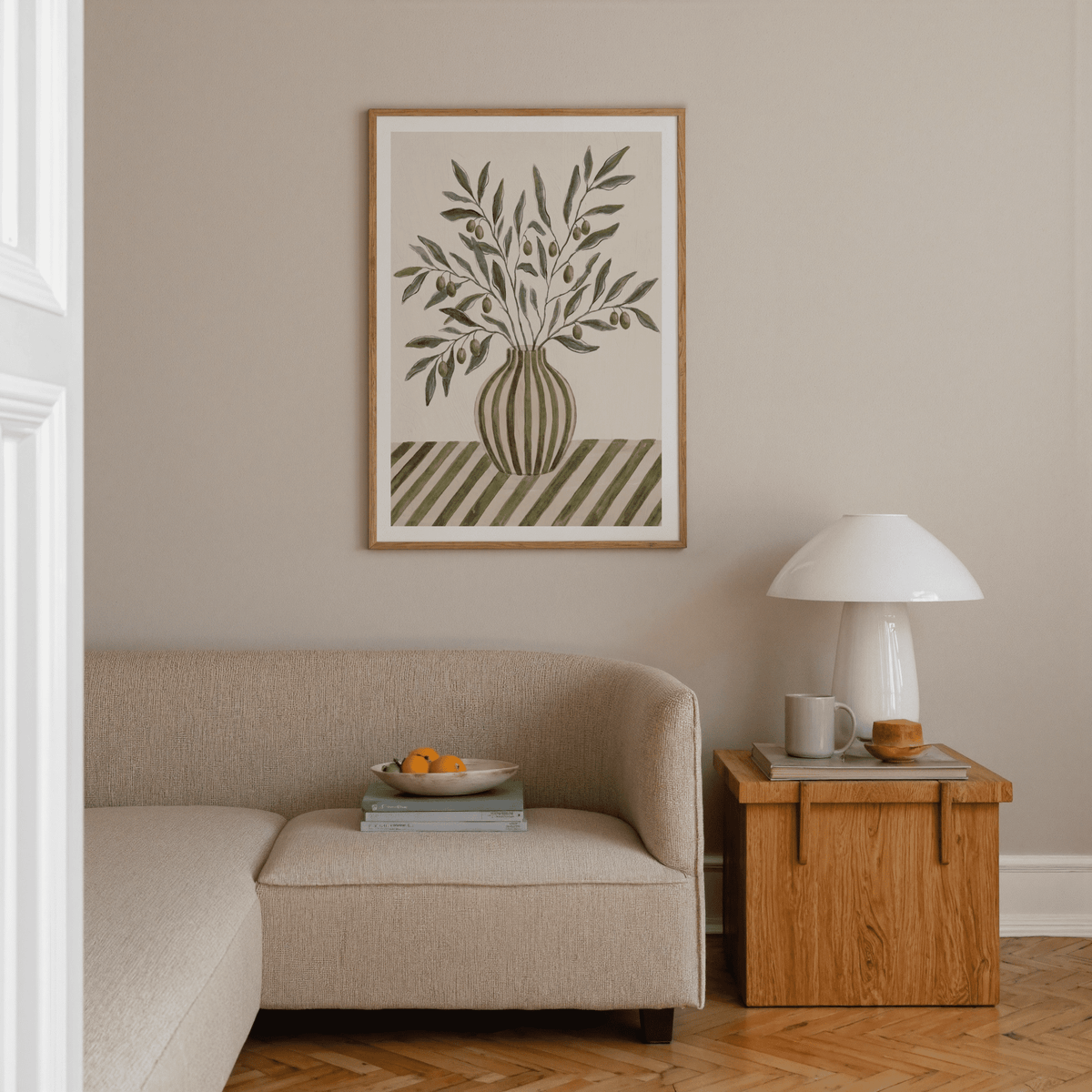 Olive Branch Art framed print on a beige wall above a corner sofa and wooden side table with lamp