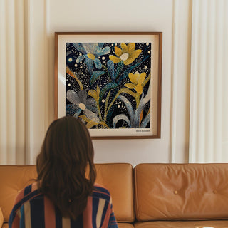 Dark floral wall art in blue and yellow above a tan leather sofa with a person sitting in front