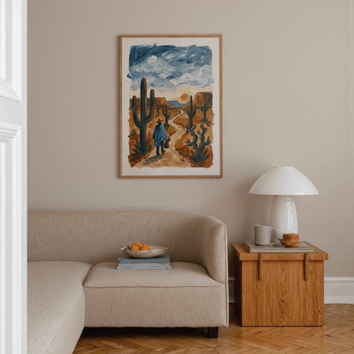 Sunset Cactus Poster Print showing a figure walking a desert path with blue skies above in a living room by a wooden side table