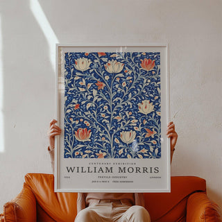 Framed Vintage Flower Wall Art held in hands above a brown leather sofa showing stylised flowers on blue background