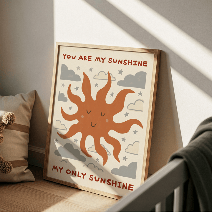 Print leaning on a floor with a minimalist smiling sun and grey clouds in warm tones near a cushion