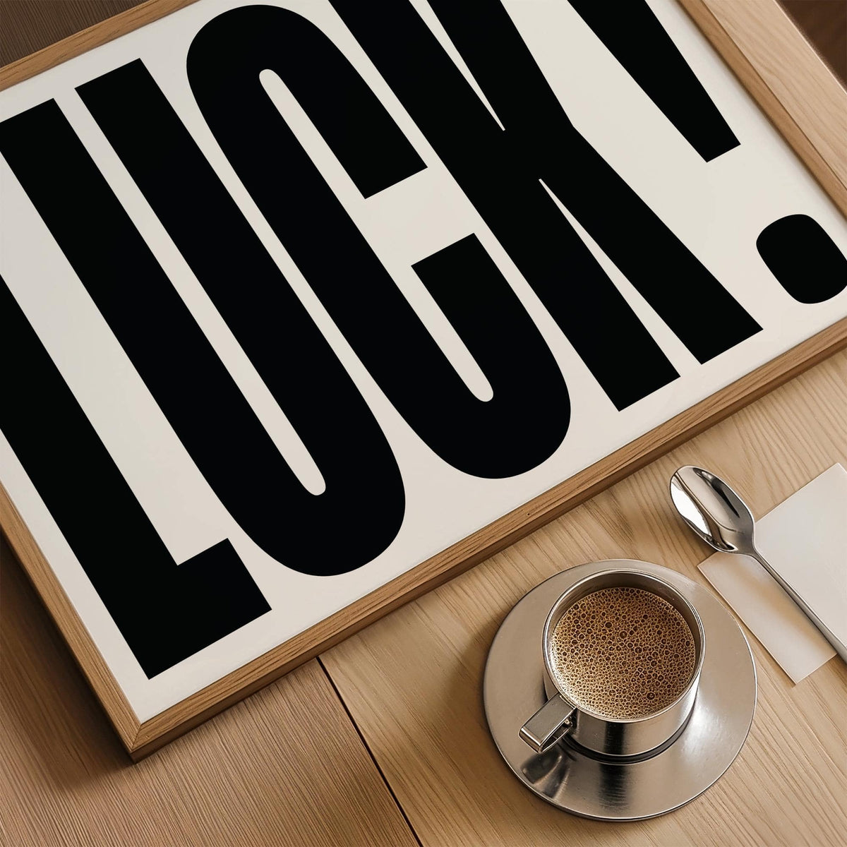 Framed Good Luck Print close-up with bold black typography and coffee cup on wooden surface