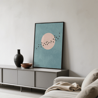 Print leaning on a shelf of wall art birds with a pink circle and blue background next to a black vase