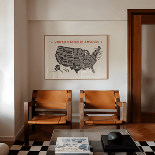 Us Map Poster on a wall above two brown leather chairs in a room with parquet flooring