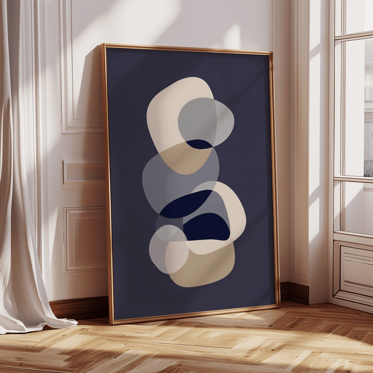 Print leaning on a floor against a wall with abstract overlapping shapes in navy, beige and grey with natural light from a window