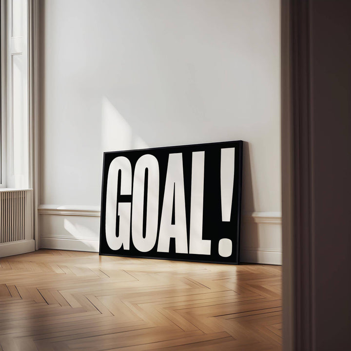 Goal Poster print leaning on the floor with black background and white bold letters in a bright room